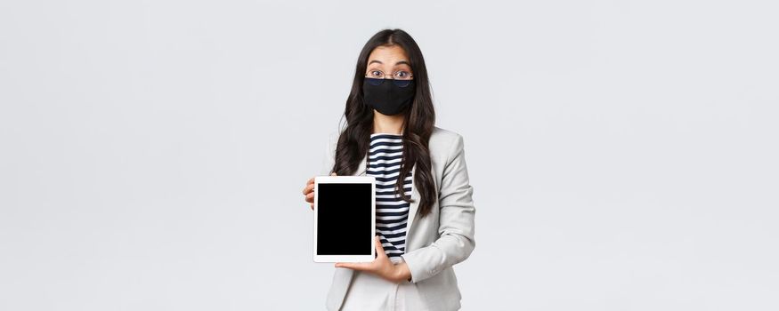 Business, finance and employment, covid-19 preventing virus and social distancing concept. Excited and surprised female office worker in face mask introduce new product on digital tablet.
