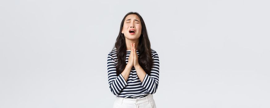 Lifestyle, people emotions and casual concept. Desperate hopeful asian girl making wish, close eyes and hold hands in pray, pleading god to have something, making wishful face, white background.