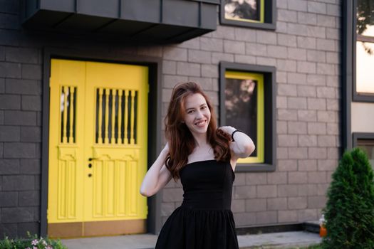 happy young woman in a black dress in front of modern building with yellow door. housewarming. buying a house. happy life in private house. new home.