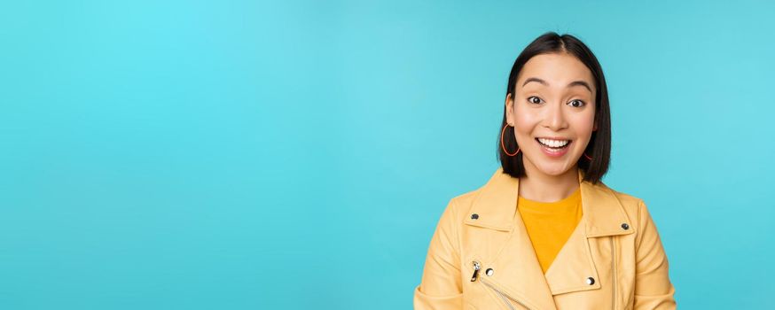 Close up portrait of asian girl looks surprised at amazed, wow face expression, stands over blue background.