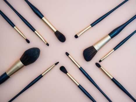 Assortment of female make-up of various face brushes. A set of professional dark blue and golden makeup brushes on a pink background. photo