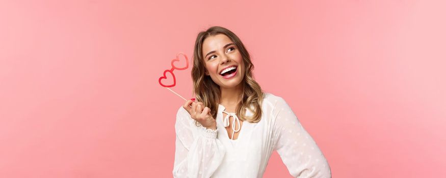 Spring, happiness and celebration concept. Close-up portrait of beautiful lovely blond girl, holding heart-shaped glasses mask and daydreaming, looking up thoughtful with pleased dreamy smile.