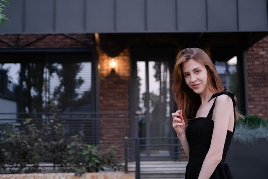 confident single woman near her new home. brown and black modern building. happy carefree suburb life.