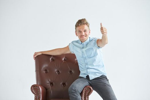 Portrait of a stylish intelligent man, small unshaven, charismatic, blue shirt, sitting on a brown leather chair, dialog, negotiation, short sleeve, brutal, hairstyle, emotions, energy, interest. High quality photo