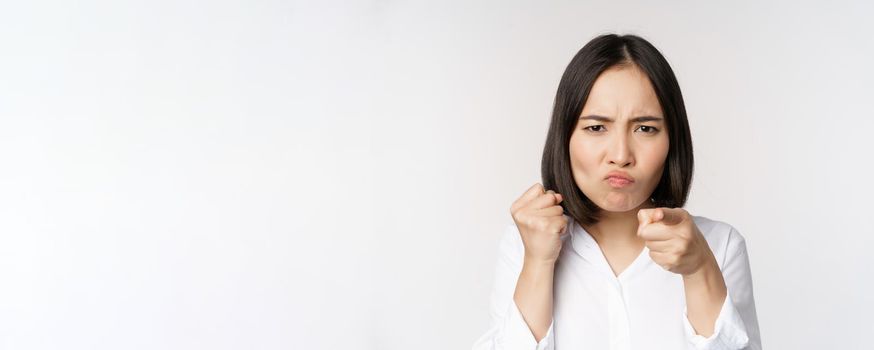 Close up of angry young woman clench fists, ready for fight, fighting, standing over white background.