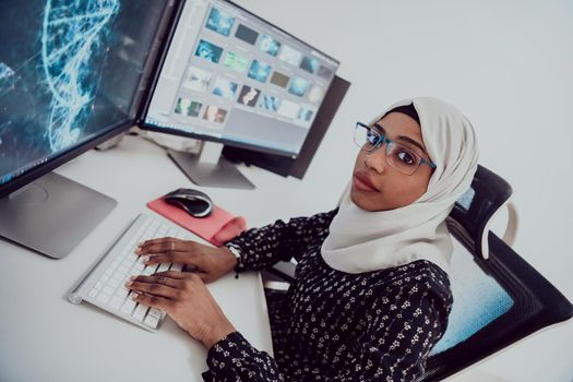 Young Afro-American modern Muslim businesswoman wearing a scarf in a creative bright office workplace with a big screen. High-quality photo