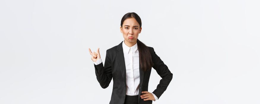Angry disappointed saleswoman in black suit complaining on small miserable size, showing something tiny and pouting displeased, standing bothered over white background. Copy space