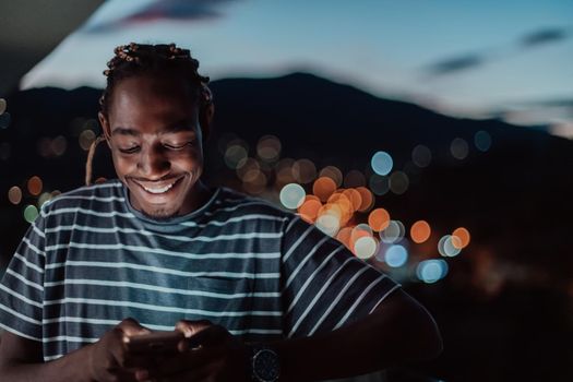 The young man on an urban city street at night texting on a smartphone with bokeh and neon city lights in the background. High-quality photo. High-quality photo