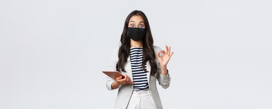 Business, finance and employment, covid-19 preventing virus and social distancing concept. Asian businesswoman with digital tablet, wear protective mask against virus and showing okay sign.
