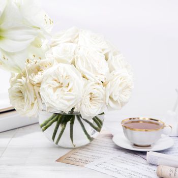 White roses, lily, in round vases with two cups of coffee on the table for a special occasion as a kitchen decoration. Copy space