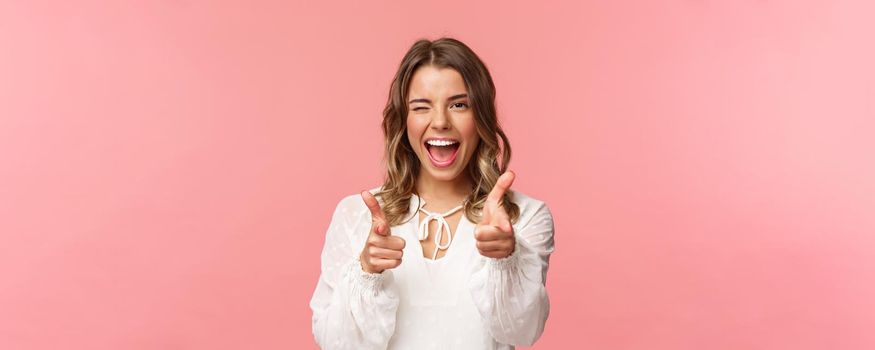 Close-up portrait of sassy and carefree good-looking emotive blond girl, pointing finger pistols at camera as asking join her team, become member, inviting try product yourself, smiling cheeky.