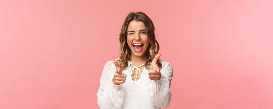 Close-up portrait of sassy and carefree good-looking emotive blond girl, pointing finger pistols at camera as asking join her team, become member, inviting try product yourself, smiling cheeky.