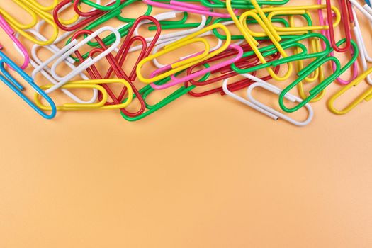 Multicolored Paperclips Isolated on a Cheerful Orange Beige Background with Copy Space on Bottom. High quality photo