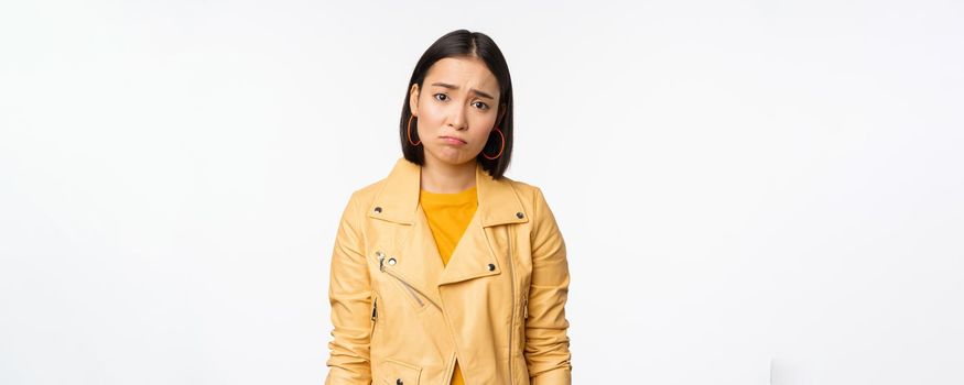Portrait of sad korean woman sulking, frowning and looking upset, distressed frustrated face expression, standing gloomy against white background.