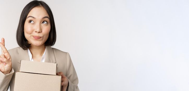 Hopeful asian entrepreneur, business woman holding boxes with customer order, making wish, wishing and anticipating, standing over white background.