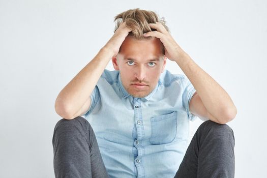 Brutal man in a shirt with short sleeves sitting on the floor, under the gaze of the forehead, holding his head. High quality photo