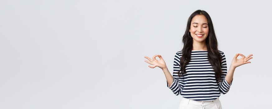 Lifestyle, people emotions and casual concept. Calm happy young woman feeling peaceful during meditation, close eyes and smiling as hold hands in zen nirvana gesture, do yoga exercise.