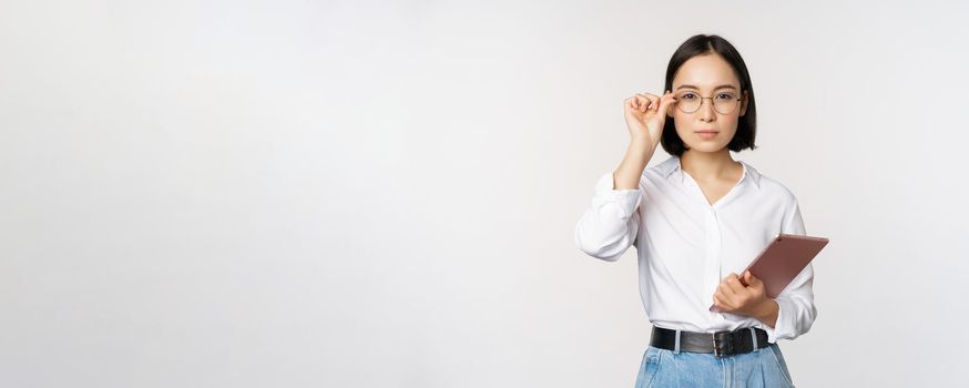 Image of young asian business woman, female entrepreneur in glasses, holding tablet and looking professional in glasses, white background.