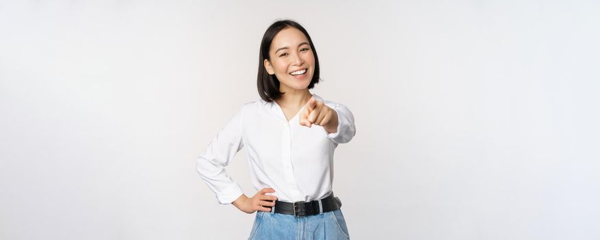 Its you. Beautiful young asian woman, company manager pointing finger at camera and smiling, choosing, inviting people, recruiting, standing over white background.
