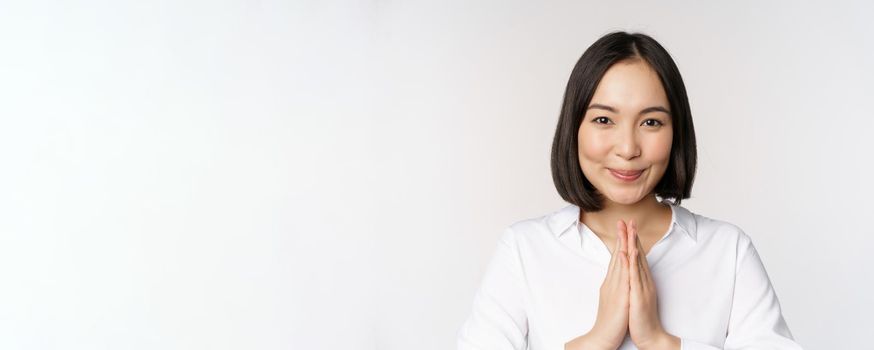 Close up portrait of young japanese woman showing namaste, thank you arigatou gesture, standing over white background.