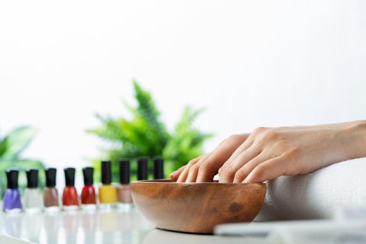 Woman hands in wooden bowl with water. Spa procedure and relaxation. Female hands preparing for manicure. Professional nail care and beautician service. Beauty and healthy lifestyle.