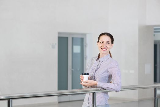 young attractive woman with a paper cup of coffee, rests on railing