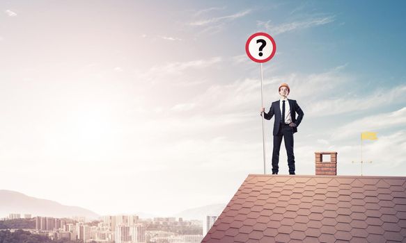 Young businessman wearing helmet with roadsign on roof edge. Mixed media