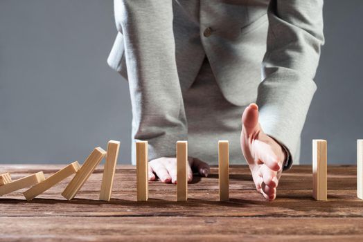 Businesswoman interrupting domino effect by stop falling wooden dominoes. Operative business solution, strategy and successful intervention. Business assistance, protection and prevention of crisis