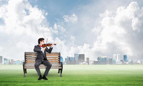 a young businessman plays the violin sitting on a wooden bench. Inspiration in business