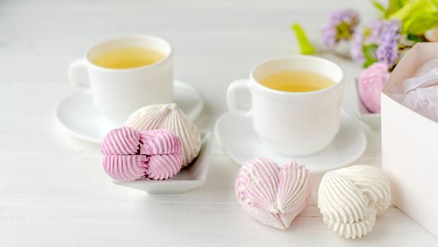 Heart shape marshmallows and cups with tea romantic composition. Craft desert sweets with beverage