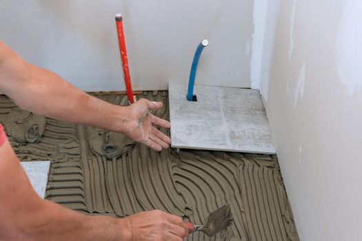 Man placing ceramic tile floor in position over adhesive