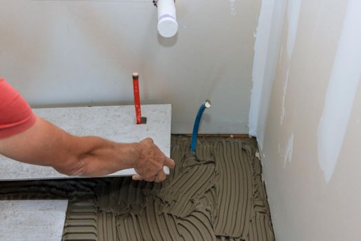 A male construction worker installs a ceramic tile on the floor