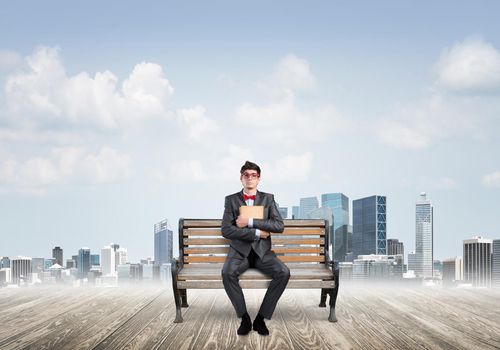 Student sits on a bench, holding a book. Traditional education concept