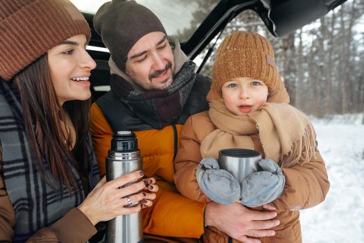 Winter portrait of a family sit on car trunk enjoy their vacation in snowy forest