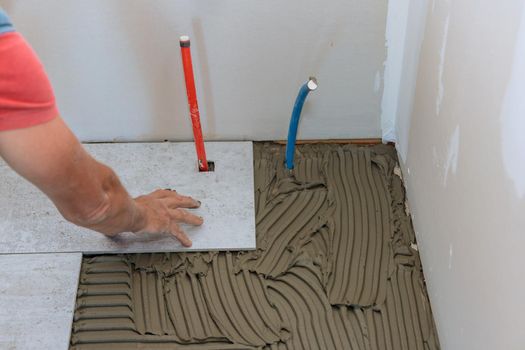 Floor tile installation witht tiler placing porcelain tile in position over adhesive