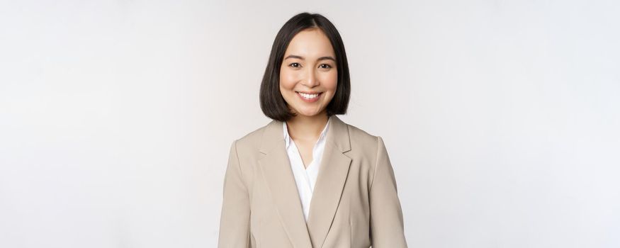 Portrait of successful businesswoman in suit, smiling and looking like professional at camera, white background.