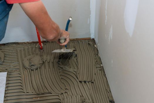 Applying adhesive base with mason trowel over floor for ceramic tile flooring