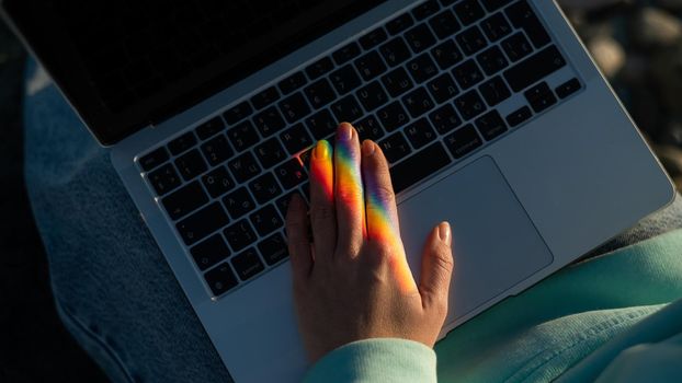 A woman is typing on a laptop. Rainbow light from a prism