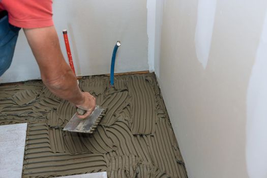 Master puts adhesive base over floor for ceramic tile