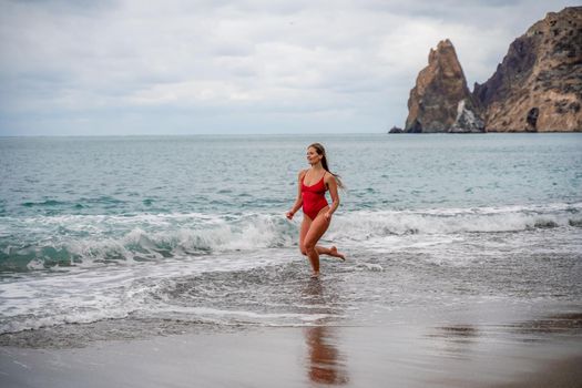 A beautiful and sexy brunette in a red swimsuit on a pebble beach, Running along the shore in the foam of the waves.