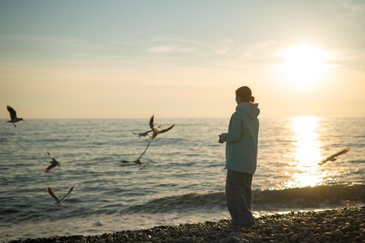 Caucasian woman feeding seagulls at sunset by the sea