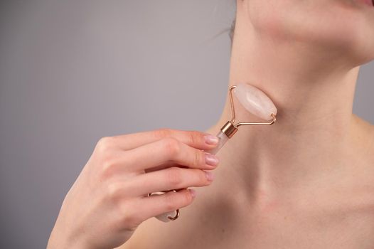 Close-up portrait of a woman using a quartz roller massager for an alternative fight against wrinkles on her neck. Smoothing of the rings of venus