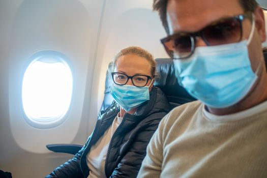 A young couple wearing face masks while traveling on airplane. New normal travel after covid-19 pandemic concept.