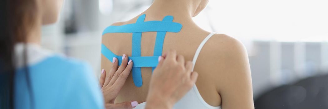 Close-up of doctor applying blue tape on patients back, problem with back, kinesiology helps fight with pain, faster recovery. Physiotherapy, rehabilitation, healthcare concept