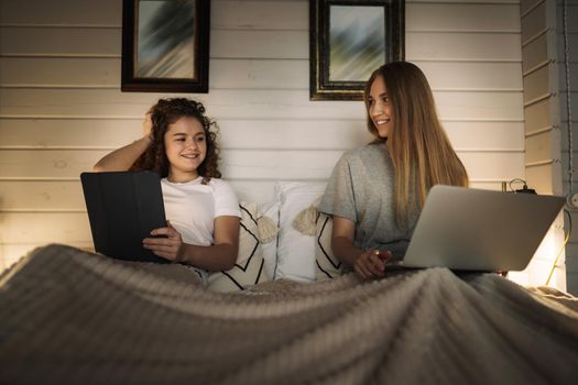Two beautiful women lying in bed, holding and watching laptop