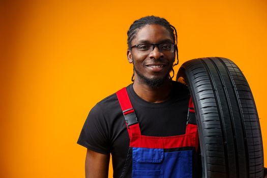 African american car service worker with car tyre against yellow background, close up