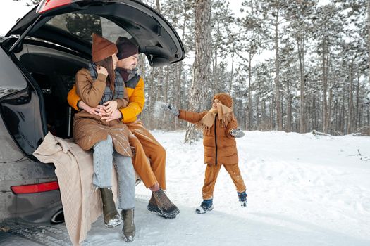 Lovely smiling couple sitting in car trunk in winter forest, close up