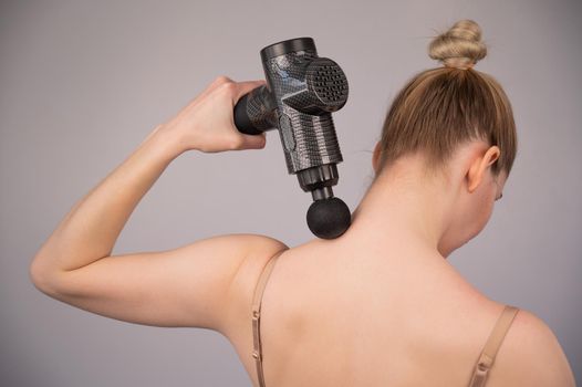 Caucasian woman giving herself a back massage with a gun