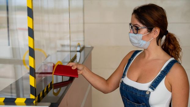 Woman in mask giving her passport at the airport check-in counter