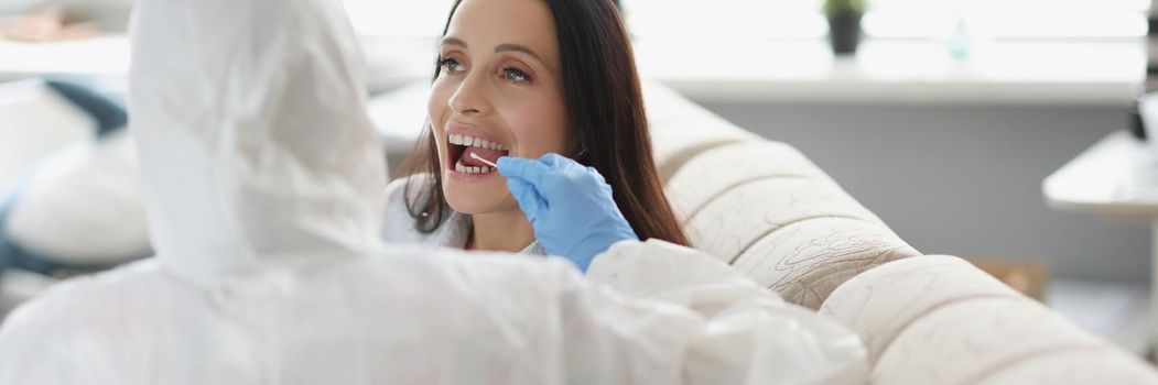 Portrait of doctor or laboratory assistant in protective suit takes swab from throat of sick patient, perform procedure at home, lab test for coronavirus. Quarantine, pandemic, health concept